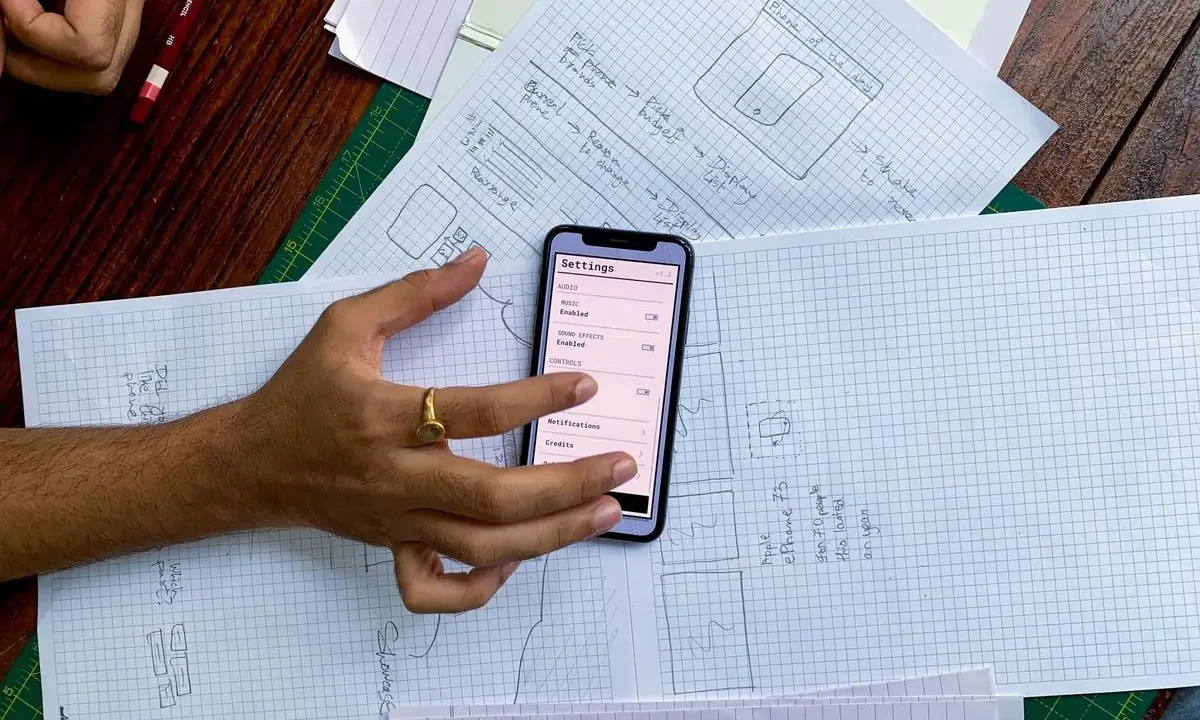 A phone held over app design sketches on a desk