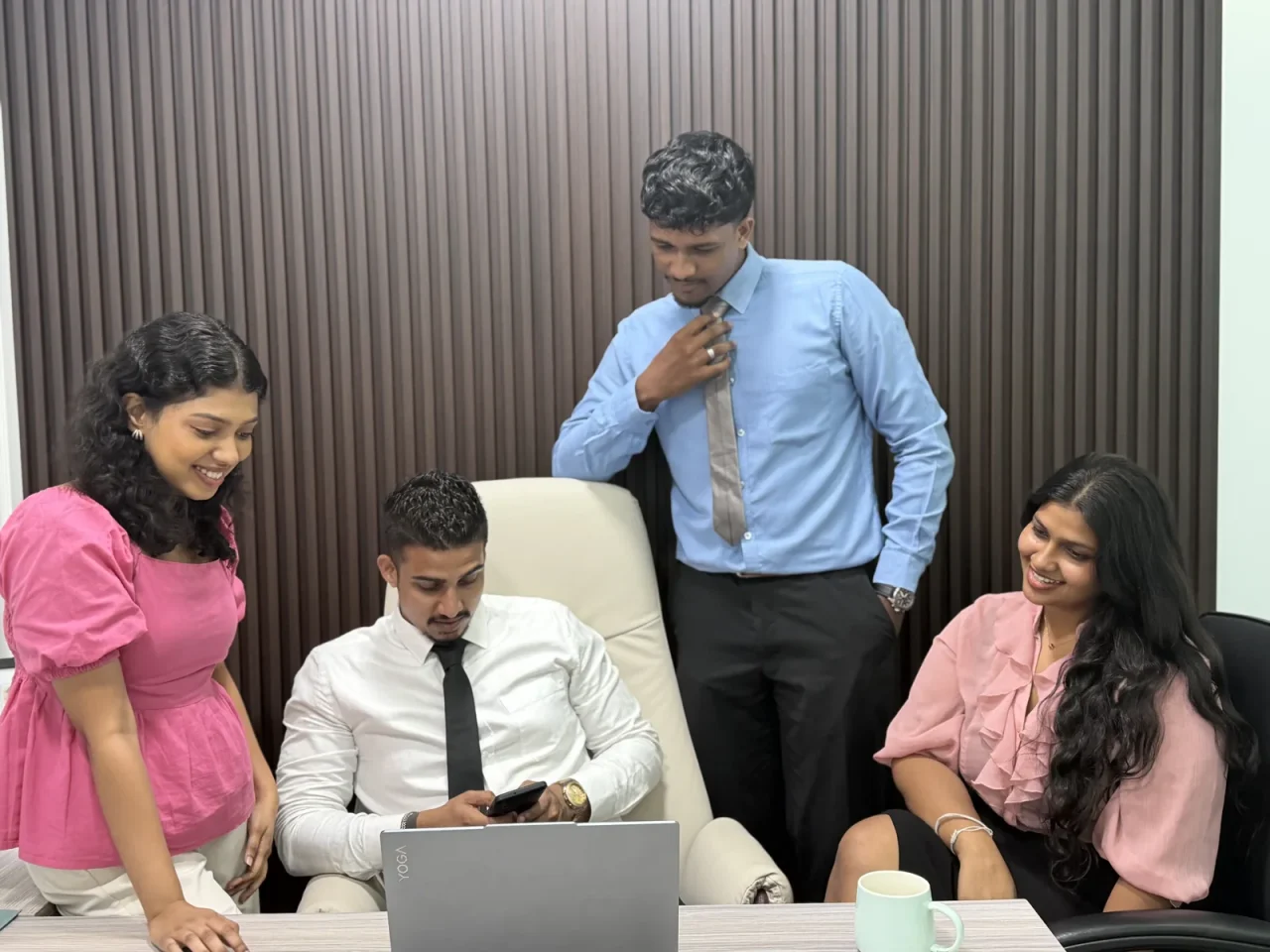 Four colleagues gathered around a laptop at a desk